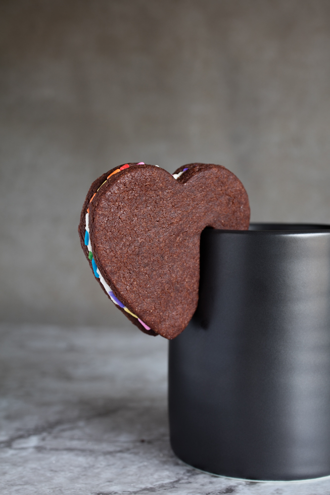 Vegan devil's food cookie sandwich perching on a cup